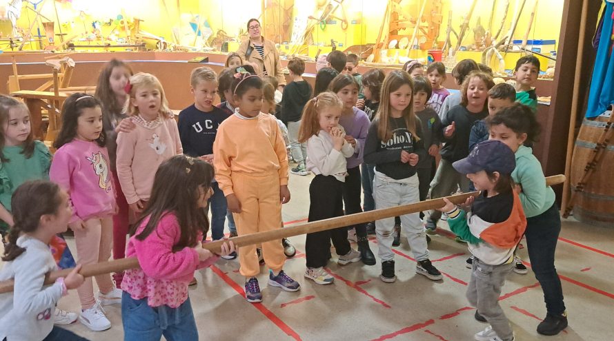 Catro alumnos xogan a un xogo tradicional que consiste en suxeitar un pao, ante a atenta mirada do resto dos seus compañeiros e unha profesora nas instalacións interiores do melga de ponteceso, museo do xogo e o deporte