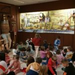 Alumnos del CEIP Bragade sentados en las instalaciones del Museo MELGA con Ricardo Pérez y Verdes de fondo